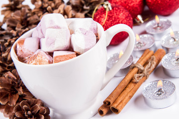 Cup of hot chocolate with marshmallows, and some cinnamon sticks, cones, christmas balls and candles	