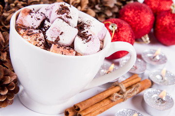 Cup of hot chocolate with marshmallows, and some cinnamon sticks, cones, christmas balls and candles	