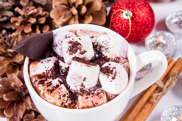 Cup of hot chocolate with marshmallows, and some cinnamon sticks, cones, christmas balls and candles	