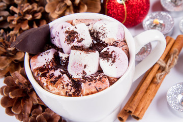 Cup of hot chocolate with marshmallows, and some cinnamon sticks, cones, christmas balls and candles	
