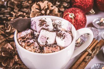 Cup of hot chocolate with marshmallows, and some cinnamon sticks, cones, christmas balls and candles	