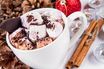 Cup of hot chocolate with marshmallows, and some cinnamon sticks, cones, christmas balls and candles	