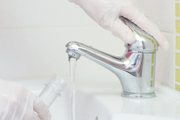 Tap water analysis quality control concept. Hand with a flask and water tap ckose up.