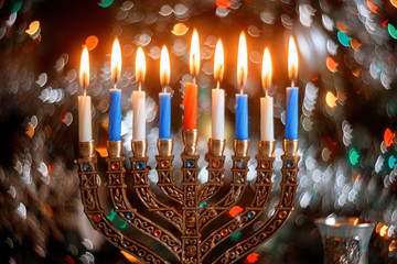 Hanukkah background with menorah and burning candles on sparkle background with defocus lights.