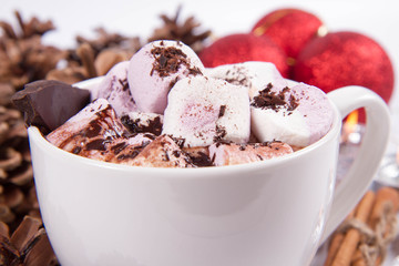 Cup of hot chocolate with marshmallows, and some cinnamon sticks, cones, christmas balls and candles	