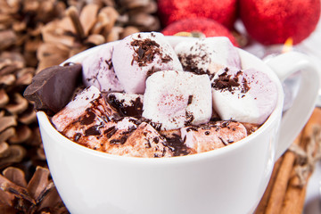 Cup of hot chocolate with marshmallows, and some cinnamon sticks, cones, christmas balls and candles	