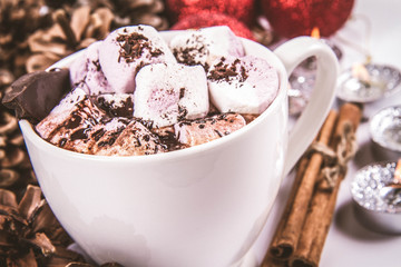 Cup of hot chocolate with marshmallows, and some cinnamon sticks, cones, christmas balls and candles	