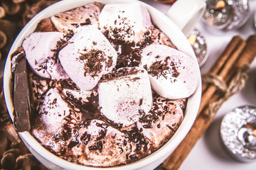 Cup of hot chocolate with marshmallows, and some cinnamon sticks, cones, christmas balls and candles	