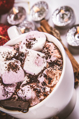 Cup of hot chocolate with marshmallows, and some cinnamon sticks, cones, christmas balls and candles	