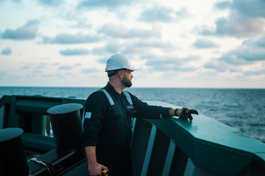Marine Deck Officer or Chief mate on deck of offshore vessel or ship , wearing PPE personal protective equipment - helmet, coverall. He holds VHF walkie-talkie radio in hands.