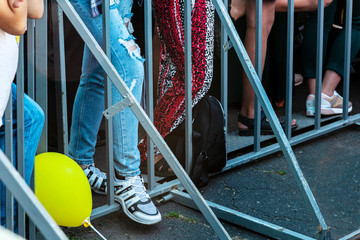The feet of music lovers stand on the railing at an entertainment event. Young people stand on a...