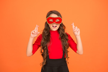 Cross fingers. Cute child make wish orange background. Little child keep fingers crossed for luck. Small child with long hair wear carnival mask. Party child. Childhood dream. Turn away the evil eye