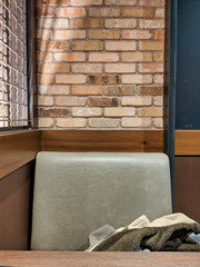 View of one side of a small, padded booth inside a brick restaurant and bar, a warm jacket slung in the seat behind a wooden table top