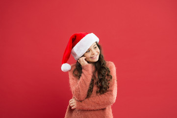 Winter traditions. Adorable girl with long curly hair wear santa claus hat red background. Counting days till christmas. Christmas party. Christmas holiday invitation. Positivity concept. Good mood