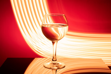 A glass with a drink on a red background with abstract yellow light lines, on a black glossy table. The concept of the holiday, new year.