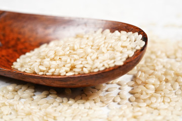 White sesame - Sesamum indicum - seeds in small wooden spoon on white stone like board