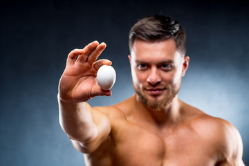 Handsome Man holding raw egg in hands showing to the camera. Attractive guy keeping healthy...