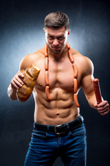 Fototapeta na wymiar man athlete with naked torso in a black background holds bread in one hand and smoked sausage in the other hand with sausages on a neck. lifestyle concept.