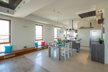 Interior of kitchen in modern studio apartment. View of wall with windows, kitchen set and laid table.