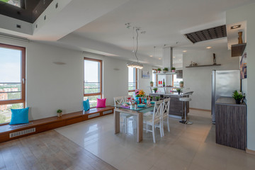 Interior of kitchen in modern studio apartment. View of wall with windows, kitchen set and laid table.