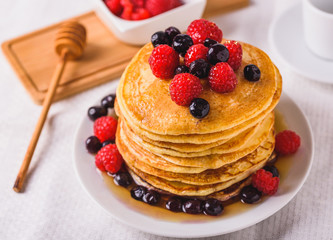 Sweet homemade pancakes with raspberries on white plate with fork.
