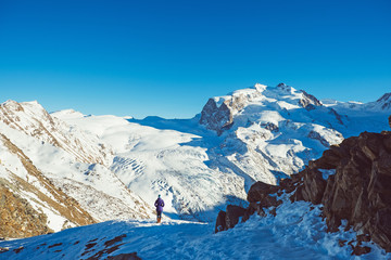 Traveler woman trekking in mountains, enjoy beautiful view. Explorer person hiking on snowy hills, travel in Swiss Alps, Switzerland. Hiker standing outdoors on nature and looking on landscape.