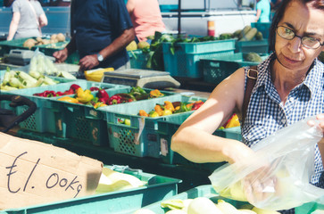 Middle-aged woman buying fresh vegetables at an open-air market stall