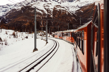 Fototapeta premium Alpine Swiss train going to the snowy Matterhorn mountain in winter. Tourists travel to mountain ski resort on railway transport from Zermatt village, Switzerland, Alps. Glacier express on the way.