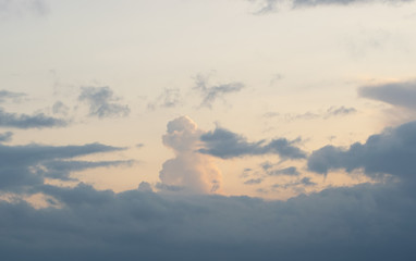 An elongated cumulus cloud illuminated by the sun rises up behind the dark evening clouds