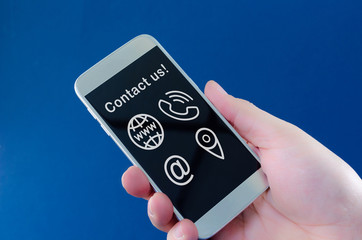 Businessman holding mobile phone with contact and communication icons glowing above it in a conceptual image. Over navy blue background.