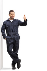 Young male worker in a uniform leaning on wall and showing thumbs up