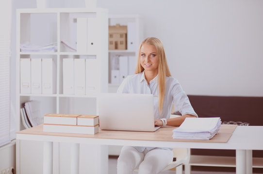 Portrait of smiling receptionist using laptop computer and headset at office desk