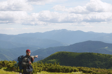 Fototapeta premium Hiker point his hand to the sun on top of a mountain enjoying valley view,The person in the foreground is blurry.