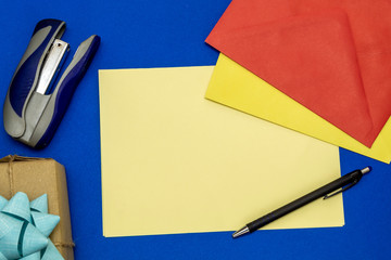 Composition Using Colorful Envelopes, Pencil, Blank Paper For Text, Gift Box, and Stapler on Blue...