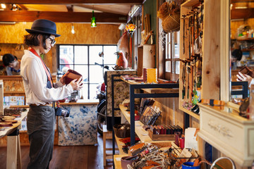Japanese woman wearing hat and glasses browsing merchandise in a leather shop.