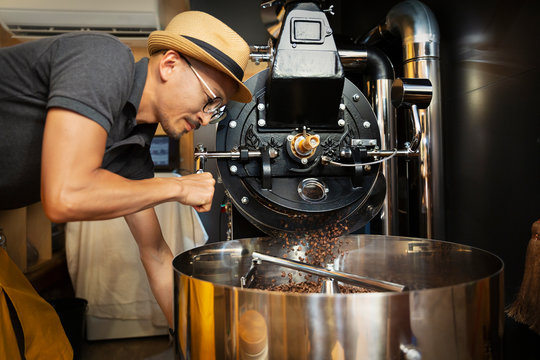 Japanese man wearing hat and glasses standing in an Eco Cafe, operating coffee roaster machine.
