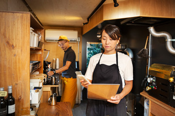 Japanese woman and man working in an Eco Cafe, preparing coffee, using mobile phone.