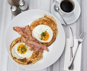 Breakfast with bacon, eggs, pancakes and coffee on white marble table