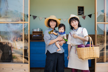Two Japanese women and boy standing outside a farm shop, smiling at camera.