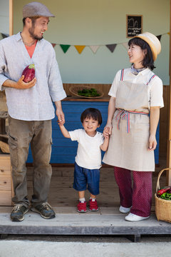 Japanese man, woman and boy standing outside a farm shop, holding hands.