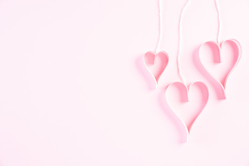 Pink paper hearts hanging on ropes on Light pink pastel paper background. Love and Valentine's day concept.