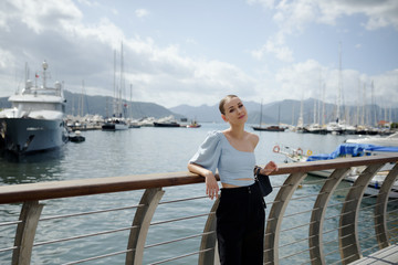 Fototapeta premium Young tourist woman on a bridge. Woman looks dreamy on the port with ships. Seascape with mountains. Summer vacation in Marmaris, Turkey. Copy space.