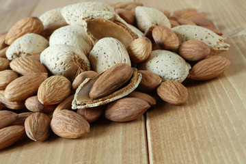 Pile of peeled raw almonds and raw almonds with shells on wooden table. Closeup