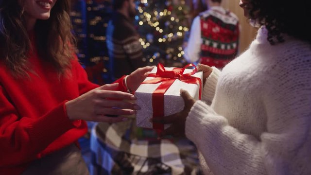 Close-up happy girl giving a handmade gift box for her friend. Surprised cheerful african woman embracing her bestie thankful for present celebrating Christmas party together.