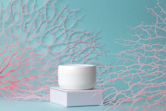 Natural facial cream healthy organic cosmetic product wellness and relaxation makeup mask in plastic white jar with branches sea corals on blue background. Face and body skin care with marine minerals