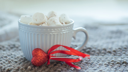 Red heart on a stick next to large cup with warm coffee or tea. Morning on Valentine's Day. pleasant surprise gift for holiday.