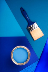 Brush on open can of blue paint on blue background. Color of the year in interior.
