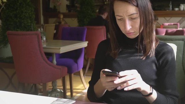 Young wonam use mobile phone while sitting in comfortable coffee shop during work break, charming happy female reading fashion news on cell telephone during breakfast in restaurant.