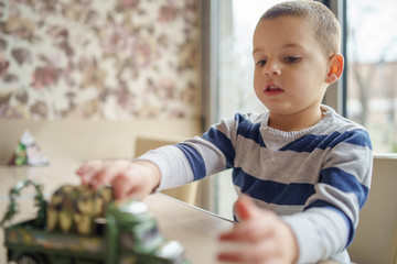 Small little boy caucasian child playing at the table by sitting in front of the window holding his toy © Miljan Živković