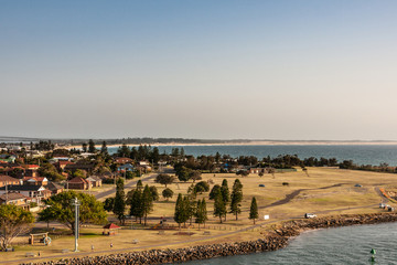 Fototapeta premium Newcastle, Australia - December 10, 2009: Looking over Stockton peninsula with its South Pacific shoreline forming a bow on the horizon under light blue to silver sky. Green foliage in front.
